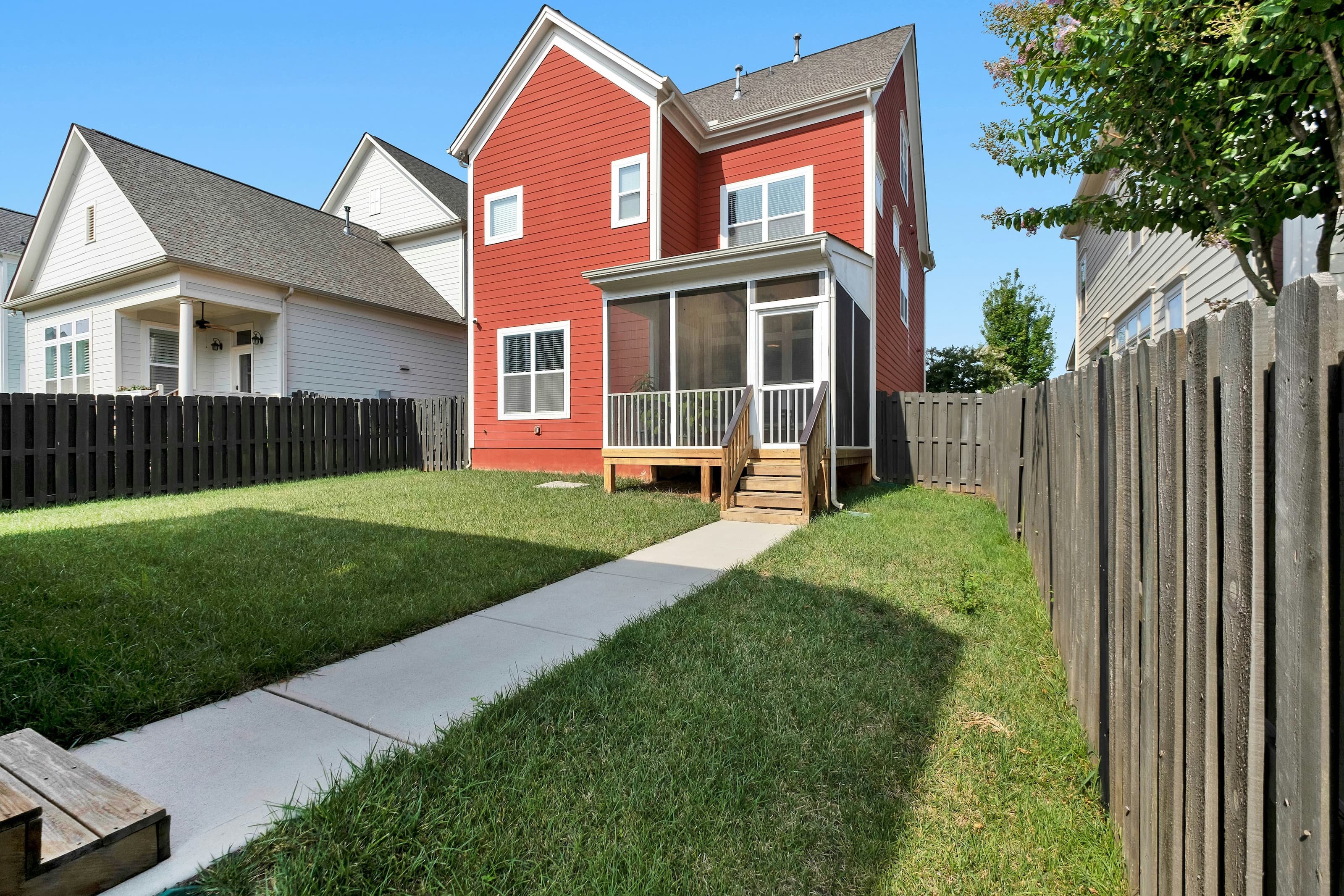 Red colored single family home with a grass covered fenced in backyard.